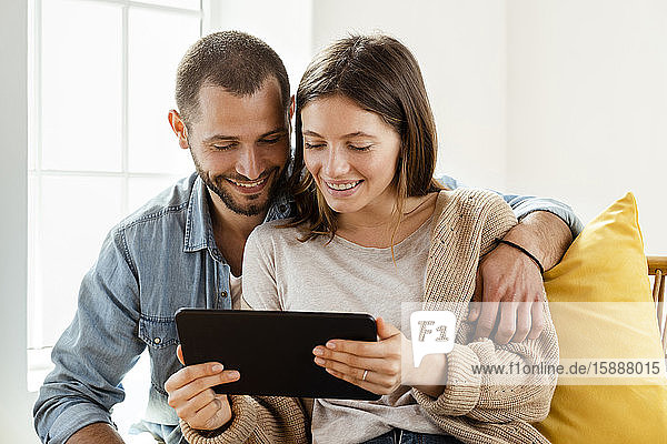 Happy couple at home in their living room in front of window looking at tablet together