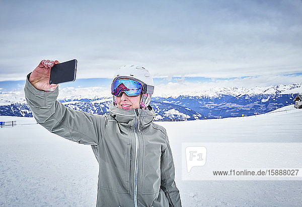 Lächelnde Snowboarderin beim Selbstfahren mit ihrem Smartphone