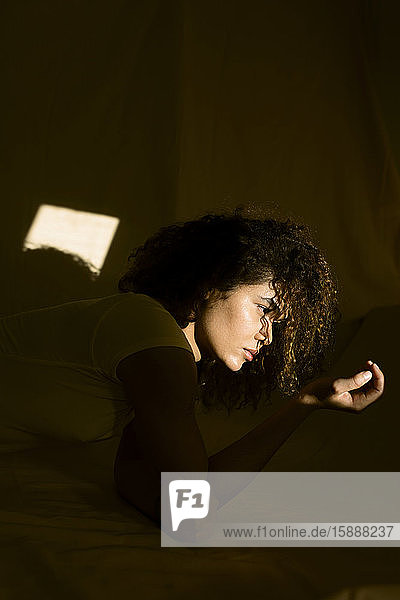 Porträt einer attraktiven jungen Frau  die im Bett im Sonnenlicht liegt