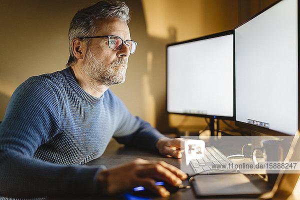 Reifer Mann sitzt zu Hause am Schreibtisch und arbeitet am Computer