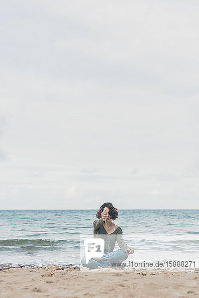Junge Frau sitzt am Strand  Sand rieselt durch ihre Hände