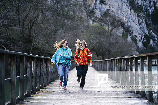 Two happy women running together on boardwalk  Valdemurio Reservoir  Asturias  Spain