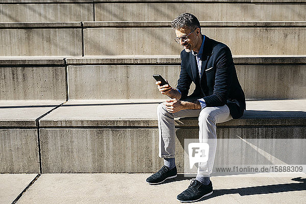 Grauhaariger Geschäftsmann sitzt auf einer Treppe und benutzt sein Handy