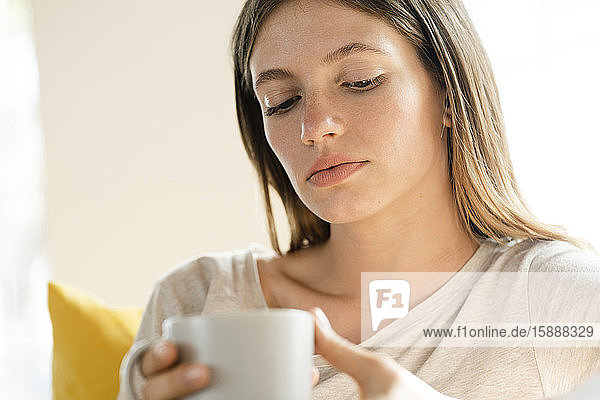 Porträt einer ernsten jungen Frau mit Kaffeetasse in der Hand