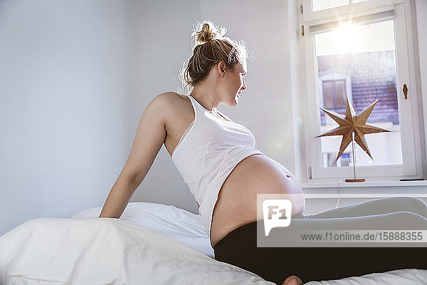 Schwangere Frau zu Hause im Bett sitzend