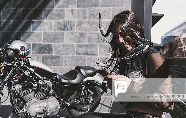 Junge Frau  die ein Smartphone neben ihrem Motorrad benutzt