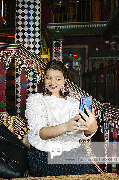 Porträt einer glücklichen jungen Frau in einem Teegeschäft  die mit einem Smartphone Selbsthilfe nimmt