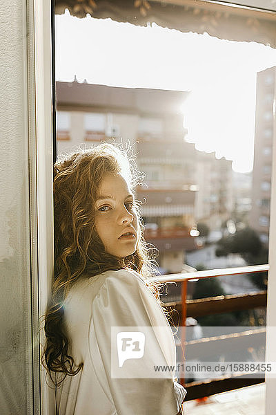 Porträt einer blonden jungen Frau an der Balkontür im Gegenlicht