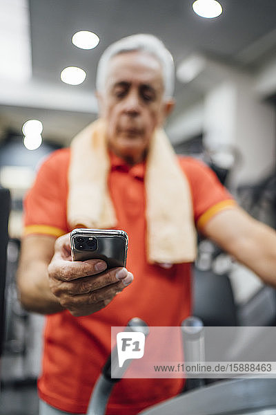 Close-up of senior man having a break and using cell phone in gym