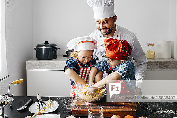 Vater mit zwei Kindern bereitet zu Hause in der Küche Teig zu