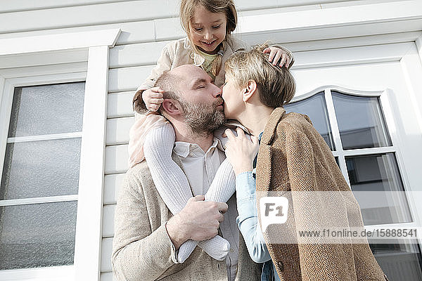 Glückliche Familie  die sich vor ihrem Haus umarmt und küsst