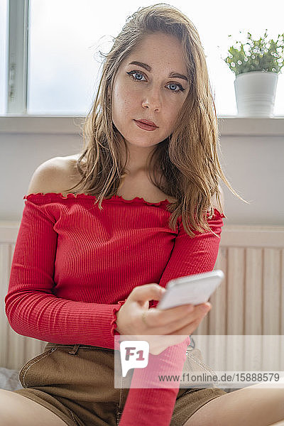 Porträt einer jungen Frau  die zu Hause ein Handy in der Hand hält