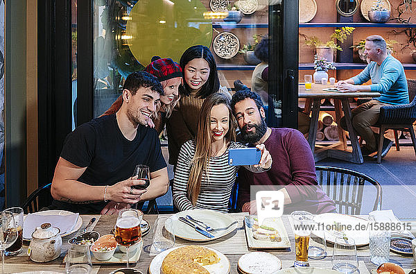 Freunde essen in einem schicken Restaurant zu Abend und nehmen sich selbst ein Smartphone