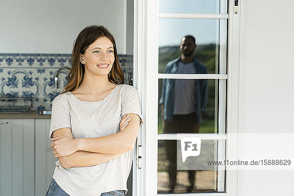 Smiling young woman leaning onto door looking at her boyfriend standing outside