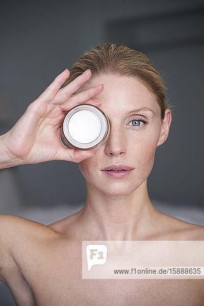 Portrait of beautiful woman holding cream jar in front of her eye