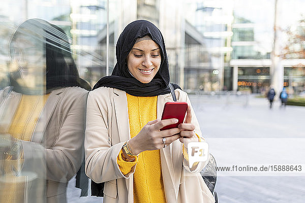 Porträt einer lächelnden jungen Frau  die ein Smartphone in der Stadt benutzt