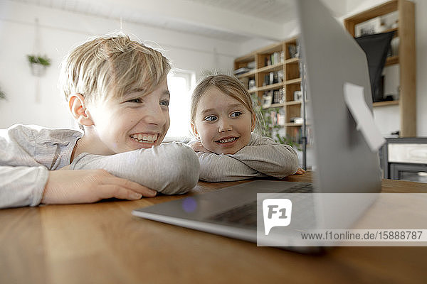 Glückliche Geschwister schauen zu Hause gemeinsam auf den Laptop