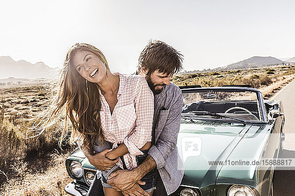 Glückliches Paar umarmt sich an einem Cabriolet auf einer Landstraße