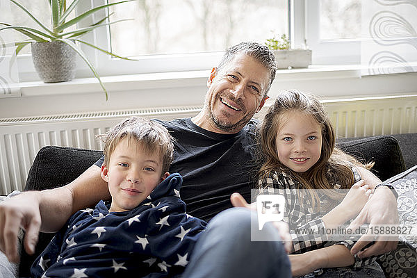 Porträt eines glücklichen Vaters mit Kindern  die sich zu Hause auf der Couch entspannen