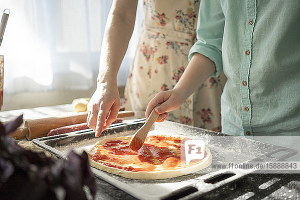 Schnittansicht eines Jungen  der Tomatensauce auf Pizzaboden streicht