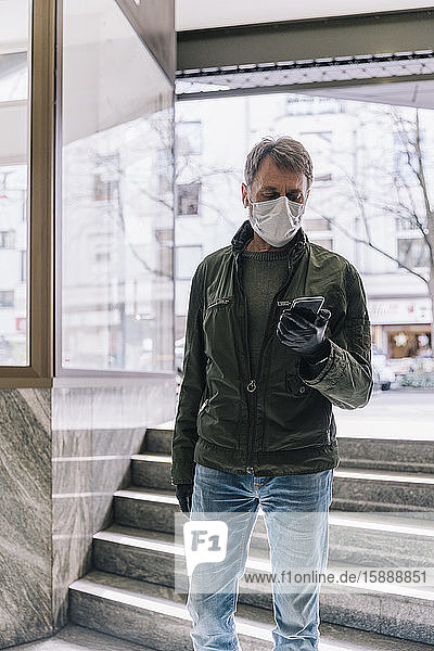 Mann mit Maske mit Smartphone auf einer Treppe in der Stadt