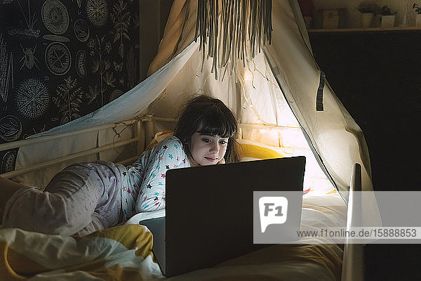 Portrait of girl lying on bed at night looking at laptop