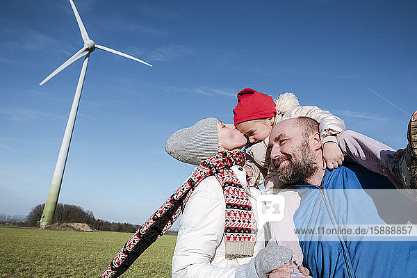 Glückliche Eltern mit kleiner Tochter gegen den Himmel mit Windrad im Hintergrund