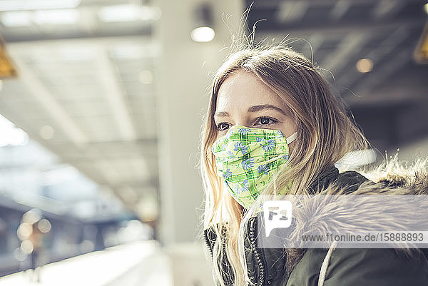 Porträt einer jungen Frau mit Maske am Bahnsteig