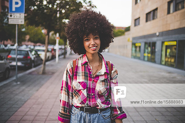 Porträt einer lächelnden jungen Frau mit Afrofrisur in der Stadt