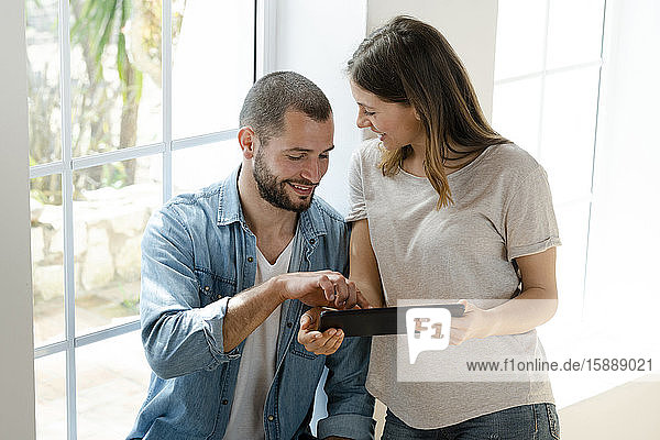 Smiling couple at home in front of window looking at tablet together