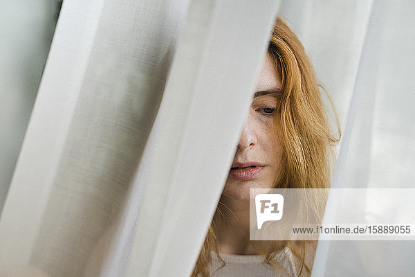 Porträt einer traurigen jungen Frau in einem Vorhang