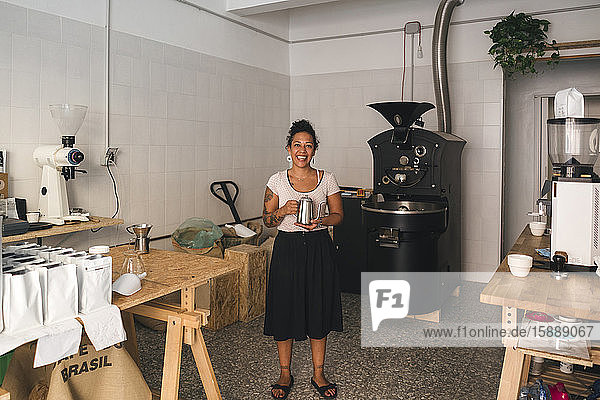 Porträt einer lächelnden Frau in einer Kaffeerösterei mit Kaffeekanne in der Hand