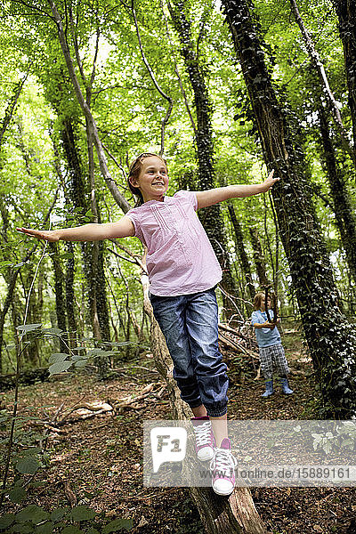 Mädchen balanciert auf Baumstamm im Wald