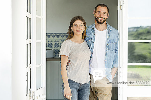 Attractive young couple standing in the door together at home and smiling
