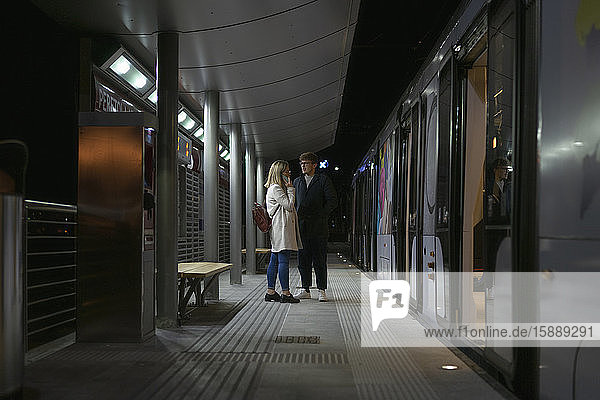 Junges Paar steht abends an der Straßenbahnhaltestelle
