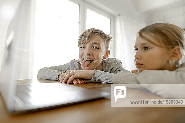 Happy brother and sister looking at laptop together at home