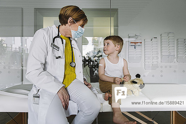 Kinderarzt mit Gesichtsmaske und Kleinkind in der medizinischen Praxis