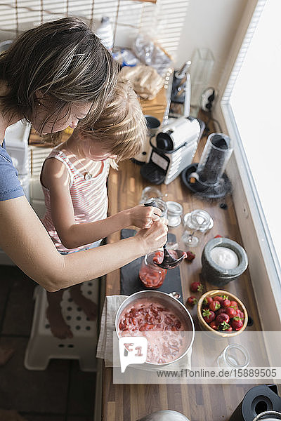 Mutter und kleine Tochter bereiten zu Hause in der Küche Erdbeermarmelade zu