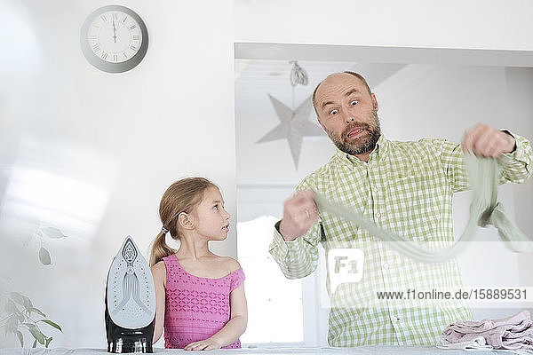 Grimacing father and daughter ironing together at home