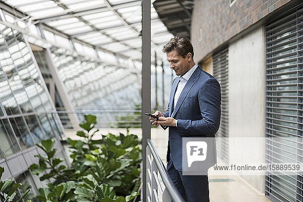Geschäftsmann mit Smartphone im grünen Atrium