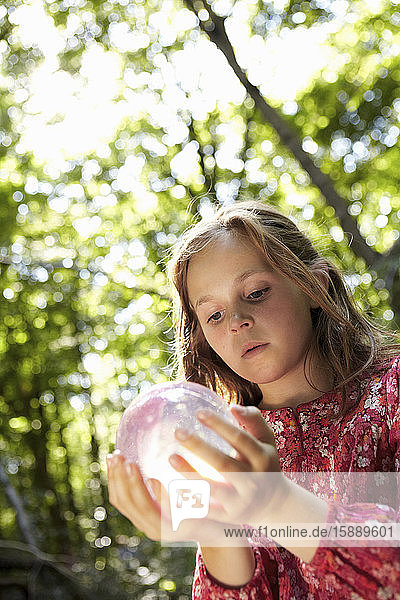 Mädchen hält Kristallkugel im Wald