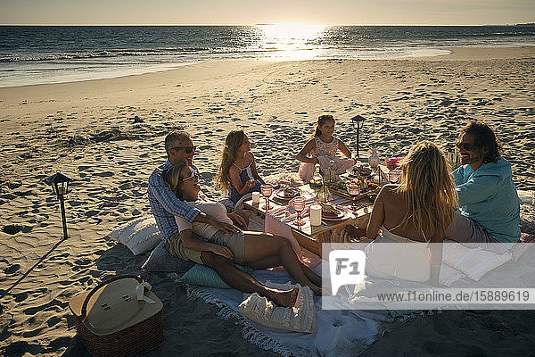 Familie und Freunde genießen ein Picknick  während sie bei Sonnenuntergang am Strand sitzen. Riviera Nayarit  Mexiko