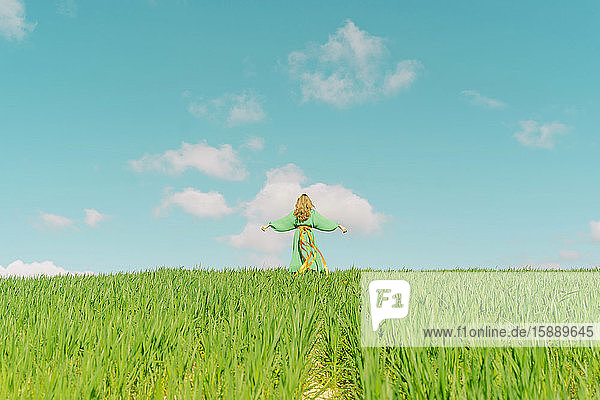 Rückansicht einer jungen Frau  die ein grünes Kleid in einem Feld mit um die Taille geschlungenen Bändern trägt