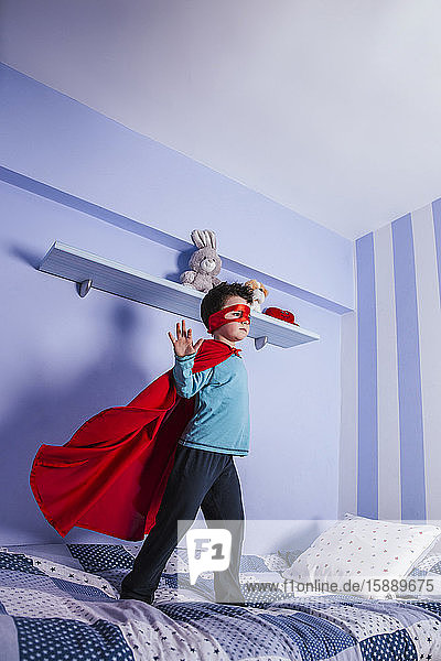 Kleiner Junge spielt Superheld und steht auf seinem Bett