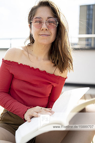 Portrait of smiling young woman reading a book on rooftop