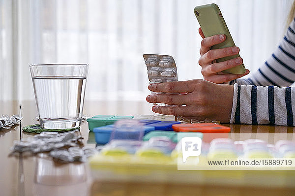 Nahaufnahme einer Frau  die Medikamente einnimmt und zu Hause ein Smartphone benutzt