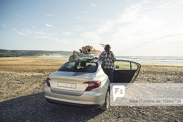 Rückenansicht einer Frau mit Auto am Strand mit Blick auf das Meer  Tafedna  Marokko