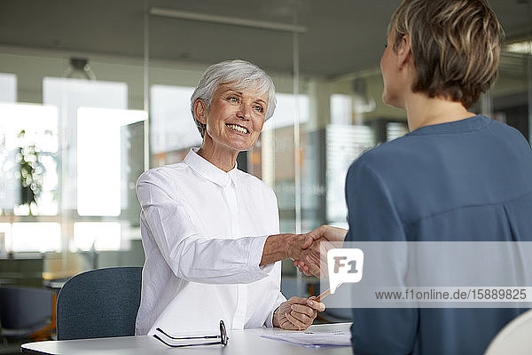 Two businesswomen shaking hands at desk in office