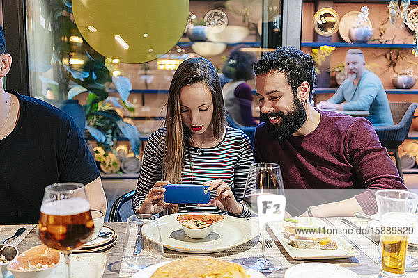 Woman taking smartphone pictures of food at a dinner with friends in a restaurant