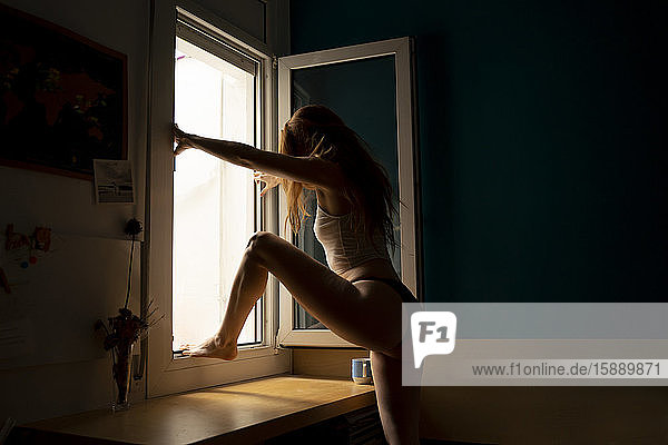 Junge Frau zu Hause klettert aus dem Fenster